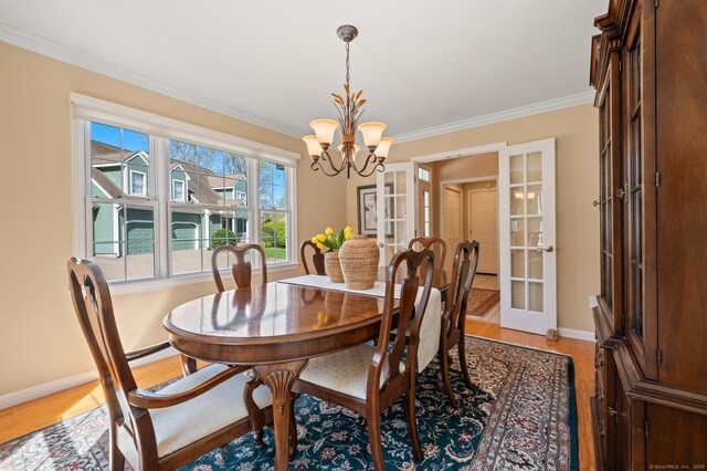 dining space with ornamental molding, a chandelier, french doors, light wood-style flooring, and baseboards