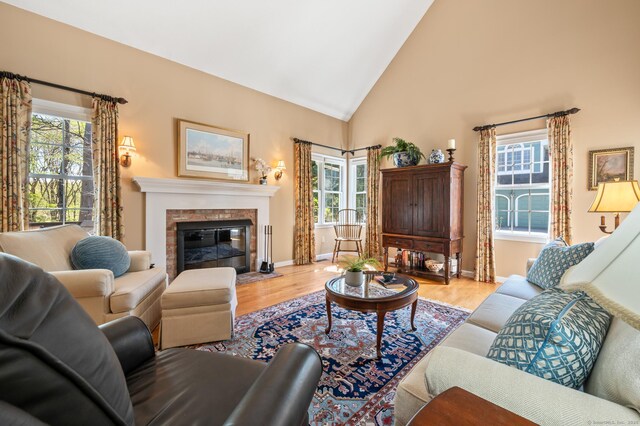 living room featuring wood finished floors, a fireplace with flush hearth, high vaulted ceiling, and baseboards