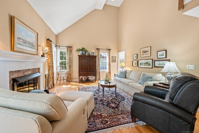 living room with light wood-type flooring, a brick fireplace, high vaulted ceiling, and baseboards