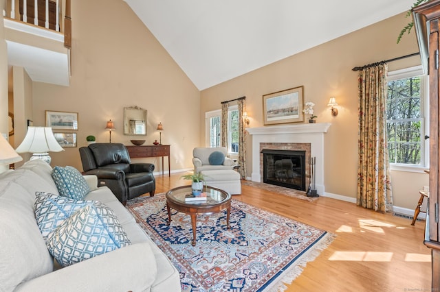 living room with wood finished floors, healthy amount of natural light, high vaulted ceiling, a fireplace with flush hearth, and baseboards