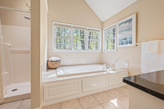 bathroom featuring healthy amount of natural light, tile patterned flooring, a shower stall, a garden tub, and vaulted ceiling