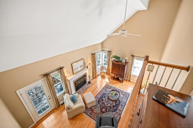 living area featuring high vaulted ceiling, wood finished floors, ceiling fan, and a fireplace with flush hearth