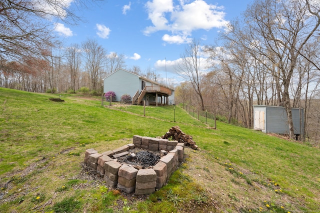 view of yard with a wooden deck, stairs, a storage unit, an outdoor fire pit, and an outbuilding
