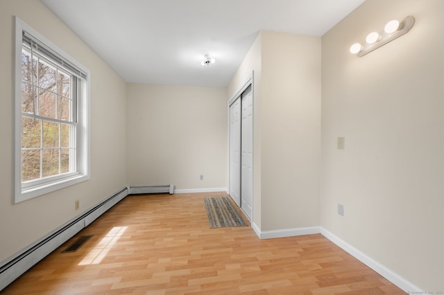 unfurnished bedroom featuring light wood-style floors, a baseboard radiator, baseboards, and a closet