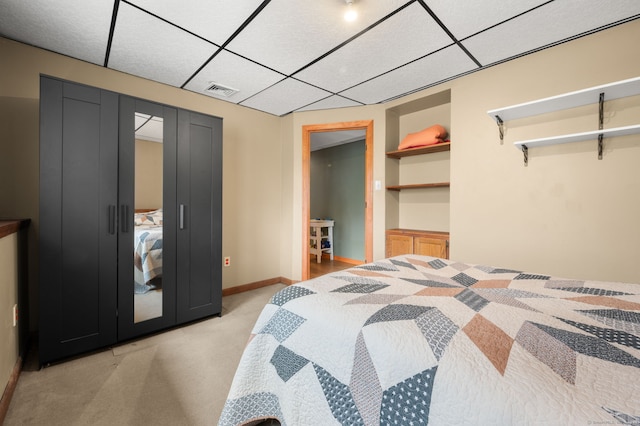 bedroom featuring light colored carpet, baseboards, a drop ceiling, visible vents, and a closet