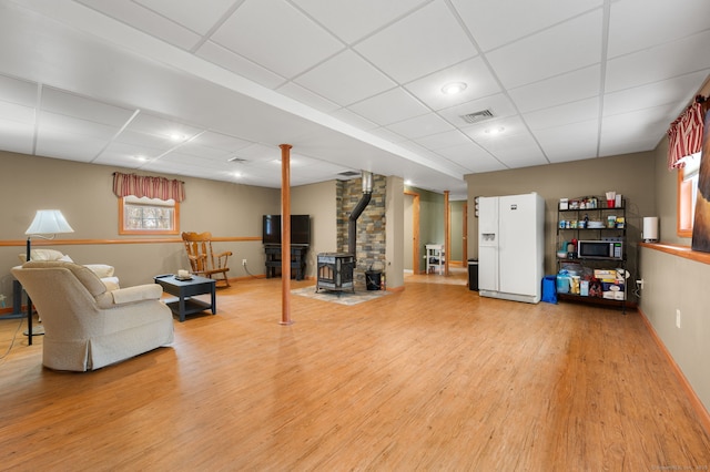 living room featuring visible vents, a wood stove, light wood-style flooring, and a drop ceiling