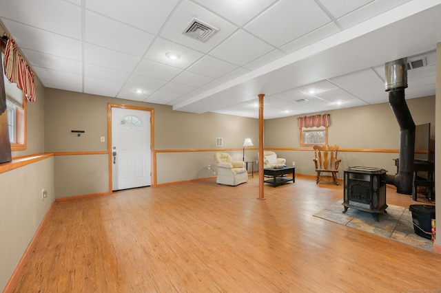 interior space featuring a paneled ceiling, a wood stove, wood finished floors, and visible vents