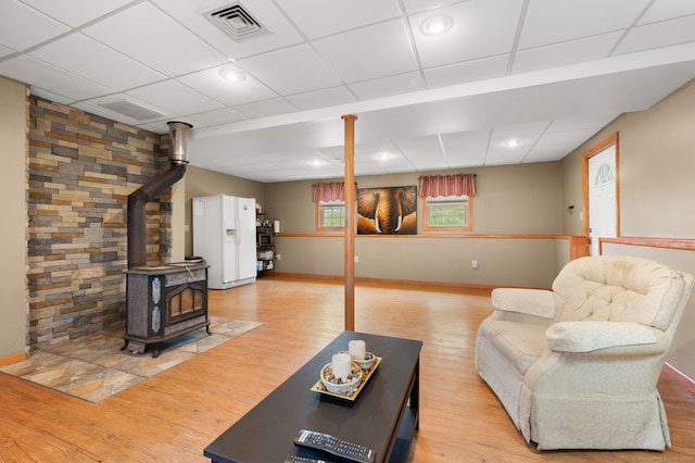 living area with visible vents, a wood stove, a paneled ceiling, and light wood-style floors