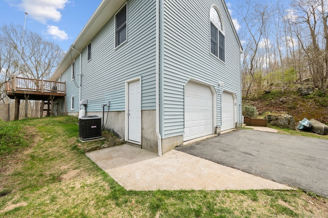 view of side of property featuring a deck, an attached garage, central AC, and aphalt driveway