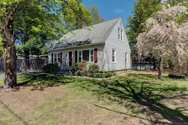 view of front of property with fence, a chimney, a shingled roof, and a front lawn