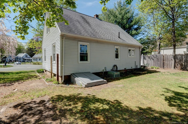 rear view of property featuring fence, a shingled roof, central AC, a chimney, and a yard