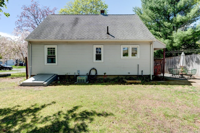 rear view of property featuring a lawn, fence, a shingled roof, and cooling unit