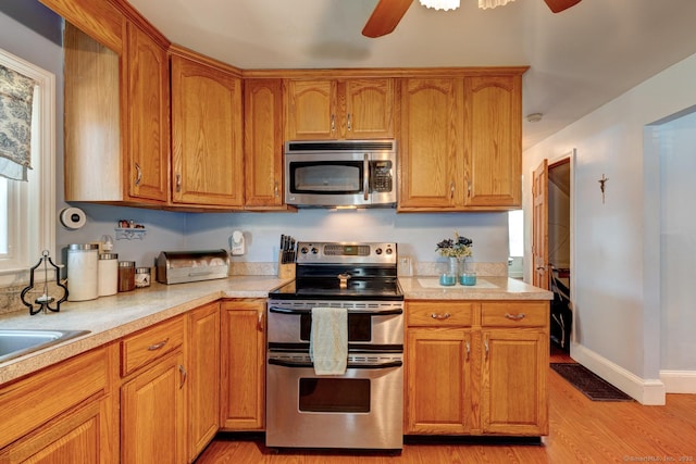 kitchen with brown cabinets, ceiling fan, appliances with stainless steel finishes, light countertops, and light wood-type flooring