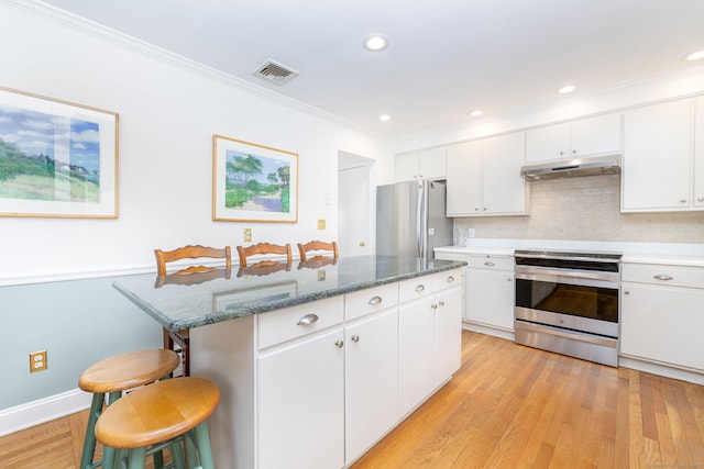 kitchen with visible vents, a kitchen breakfast bar, a center island, under cabinet range hood, and appliances with stainless steel finishes