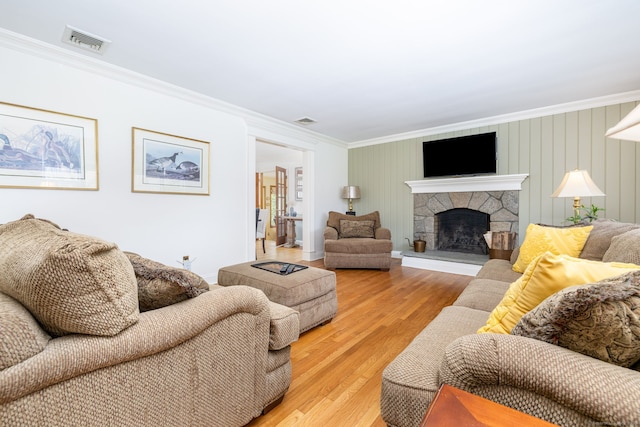 living room with visible vents, light wood-style flooring, crown molding, and a stone fireplace