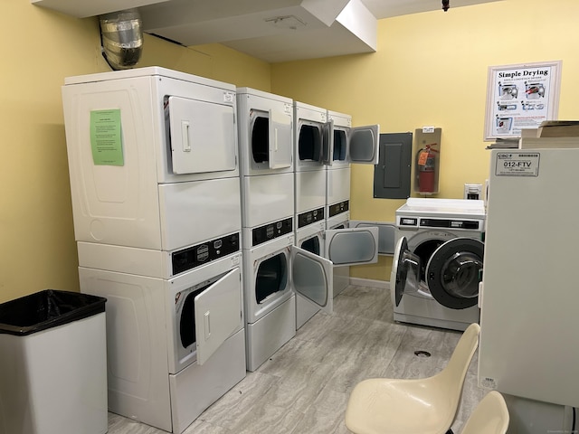 common laundry area with electric panel, independent washer and dryer, light wood finished floors, and stacked washer / drying machine