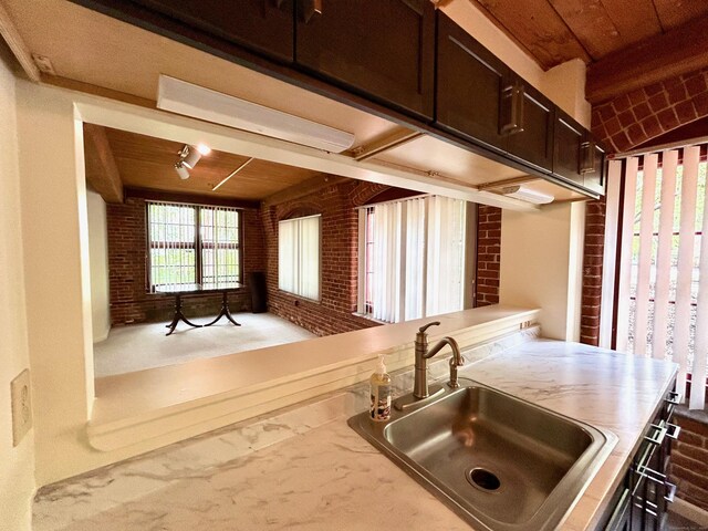 kitchen featuring a sink, light countertops, brick wall, and wooden ceiling