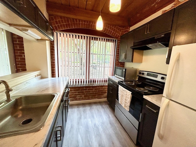 kitchen with a sink, stainless steel range with electric stovetop, freestanding refrigerator, under cabinet range hood, and brick wall