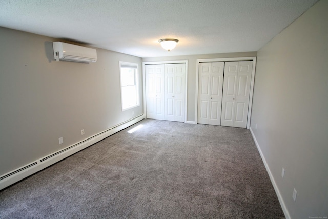 unfurnished bedroom with two closets, a textured ceiling, a baseboard heating unit, a wall mounted AC, and carpet flooring