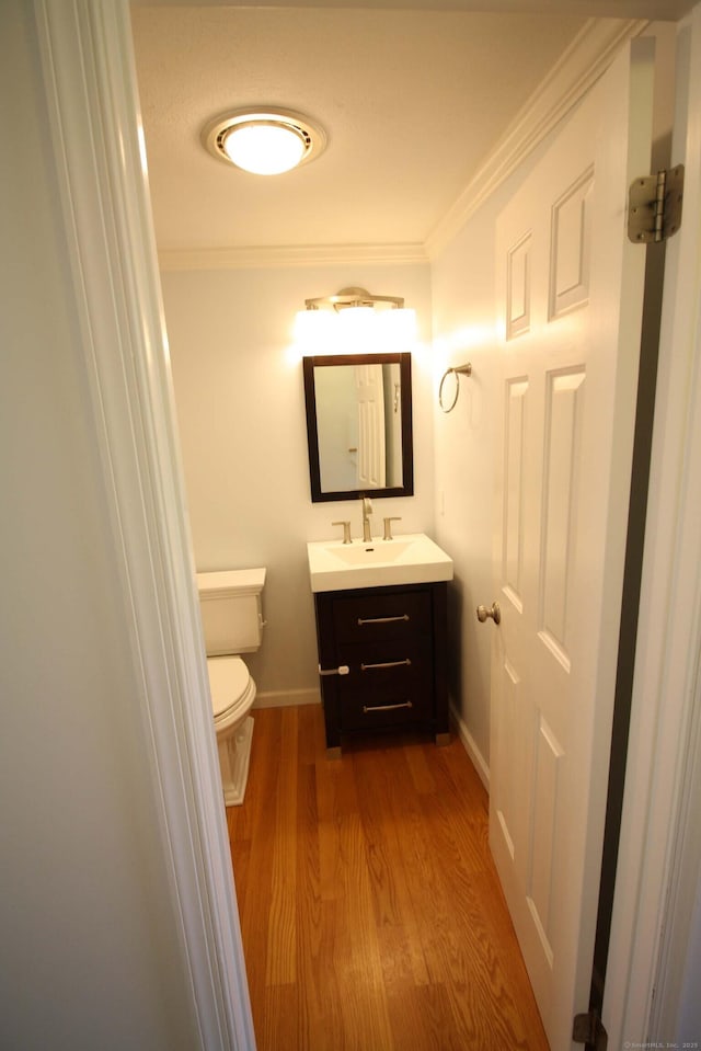 bathroom featuring vanity, ornamental molding, wood finished floors, toilet, and baseboards