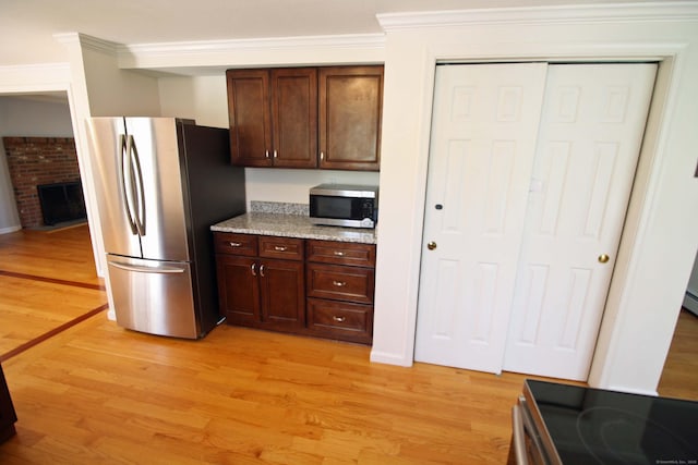 kitchen featuring light stone countertops, a brick fireplace, dark brown cabinets, stainless steel appliances, and light wood-style flooring