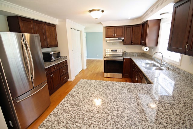 kitchen with light stone countertops, a sink, light wood finished floors, under cabinet range hood, and stainless steel appliances