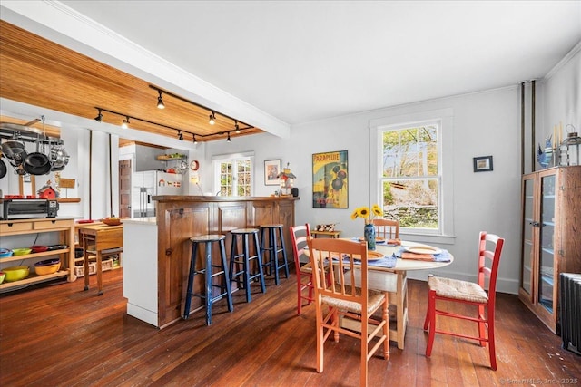 dining space featuring rail lighting, ornamental molding, and hardwood / wood-style flooring