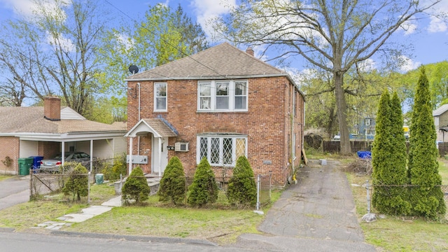 traditional-style home with driveway, brick siding, fence, a front lawn, and a shingled roof