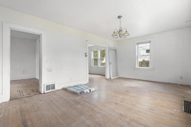 spare room featuring baseboards, visible vents, wood-type flooring, and a chandelier