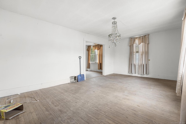 spare room featuring baseboards, a notable chandelier, and wood finished floors