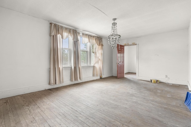 unfurnished room with baseboards, wood-type flooring, and a notable chandelier