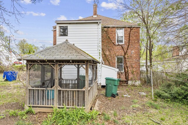 back of house with a sunroom, a shingled roof, a chimney, and a gazebo