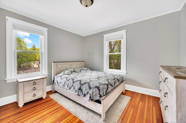 bedroom with baseboards, multiple windows, ornamental molding, and wood finished floors