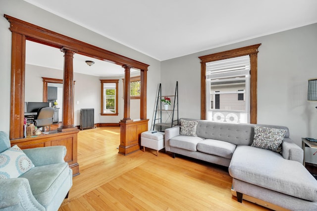 living room with baseboards, decorative columns, light wood finished floors, and radiator heating unit
