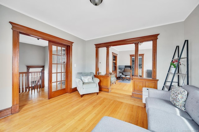 living room featuring ornamental molding, radiator, decorative columns, wood finished floors, and baseboards
