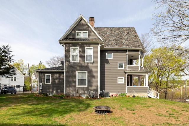 back of house featuring a chimney, a yard, a fire pit, central air condition unit, and a balcony
