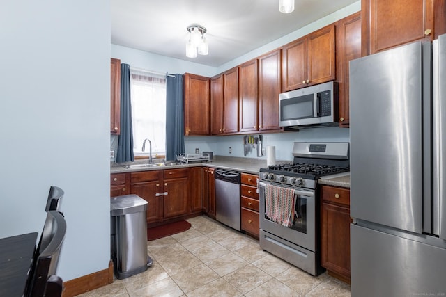 kitchen featuring appliances with stainless steel finishes, light tile patterned floors, brown cabinets, and a sink