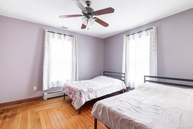 bedroom featuring hardwood / wood-style flooring, visible vents, a baseboard heating unit, baseboards, and a ceiling fan