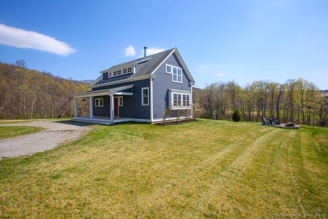 view of front of property with a porch, a wooded view, a front yard, and gravel driveway