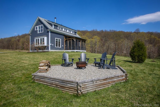 back of house with a sunroom, a view of trees, a fire pit, and a yard