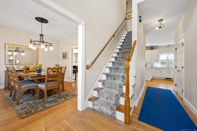 dining area featuring baseboards, a notable chandelier, light wood finished floors, and stairway
