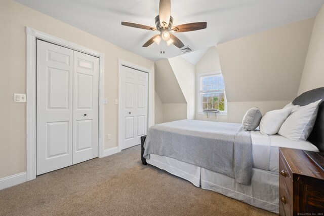 bedroom with carpet floors, visible vents, two closets, baseboards, and vaulted ceiling