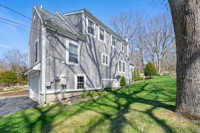 view of side of home featuring a lawn, an attached garage, and driveway