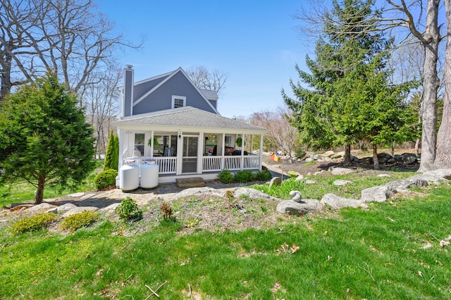 rear view of property with roof with shingles, covered porch, and a chimney