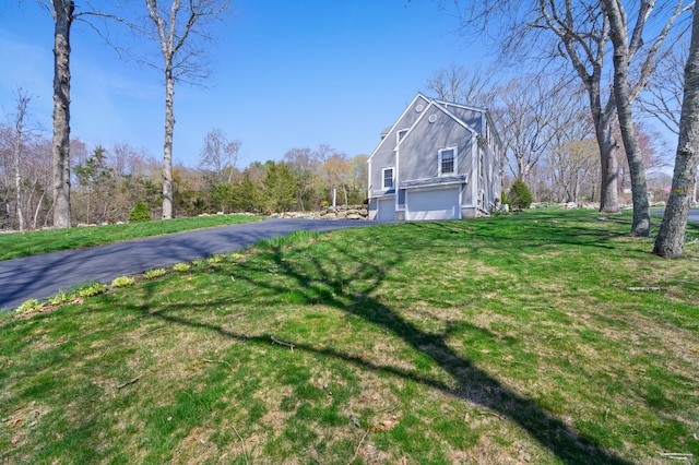 view of side of home featuring an attached garage, a yard, and driveway