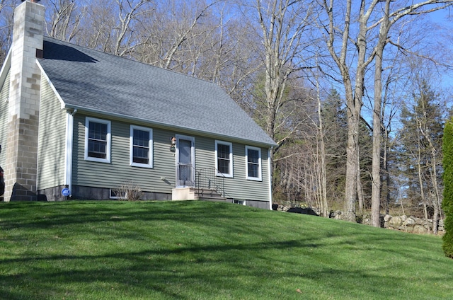 cape cod-style house featuring a chimney, a front lawn, and a shingled roof