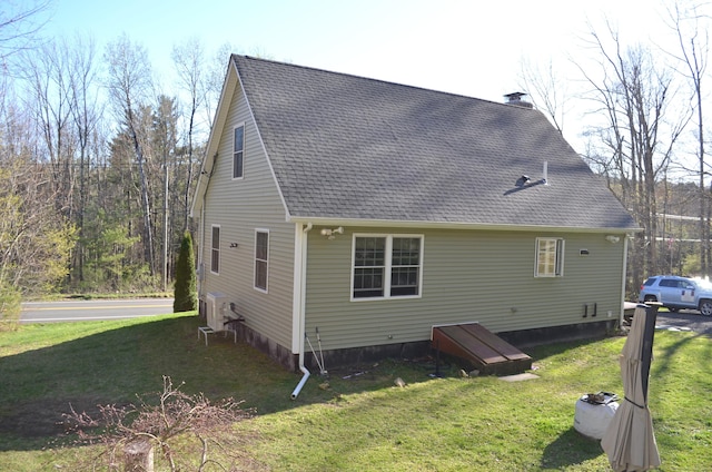 back of house featuring roof with shingles and a lawn