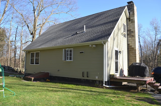 rear view of house featuring a chimney, roof with shingles, and a lawn