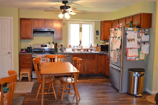 kitchen with under cabinet range hood, brown cabinetry, dark wood-type flooring, a ceiling fan, and appliances with stainless steel finishes