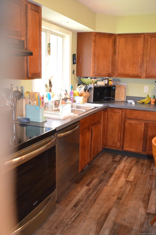 kitchen featuring a sink, appliances with stainless steel finishes, brown cabinetry, and dark wood-type flooring